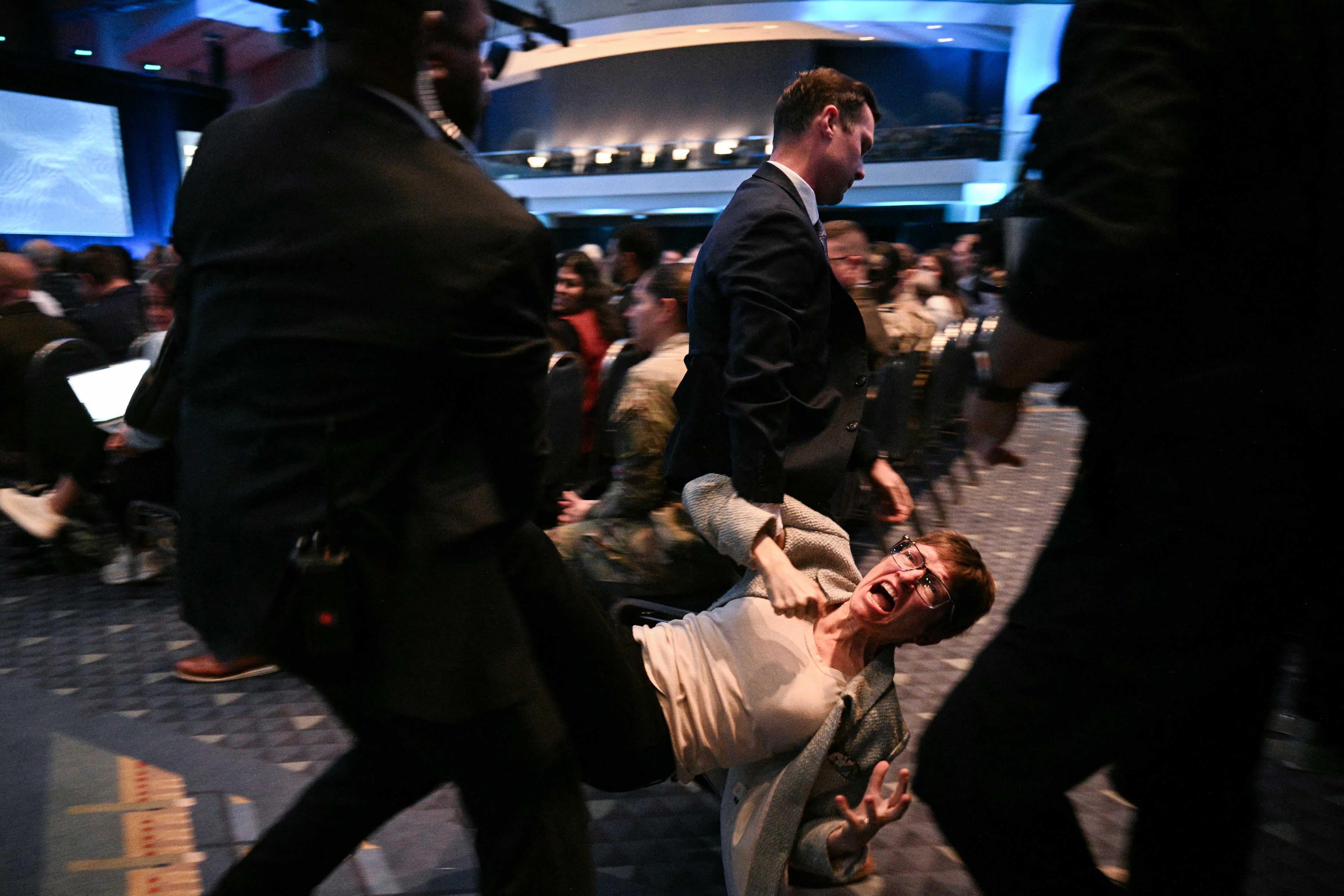 A woman protester is carried out of the AUSA panel by officers